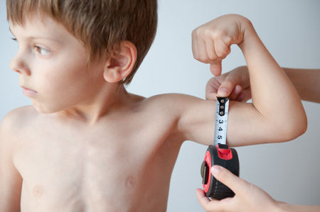 child measures healthy little boy muscles with measuring tapeの写真素材