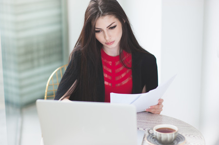 pretty young female holding documents and work with laptop in cafeの写真素材