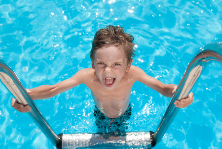 handsome funny boy in blue azure pool in summer sunny day outdoorの写真素材