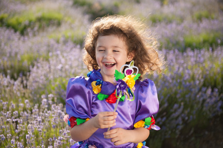 happy delightful beautiful little girl in fairy dress and magic wand in hand in summer fieldの写真素材