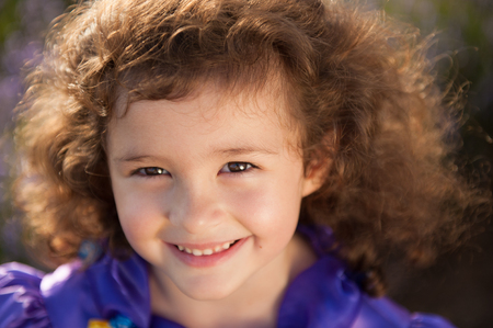 portrait of smiling beautiful little girl with brown curly hair blown by summer windの写真素材