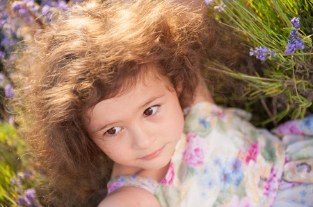 beautiful face of little caucasian girl with curly hair lying among lavender summer fieldの写真素材