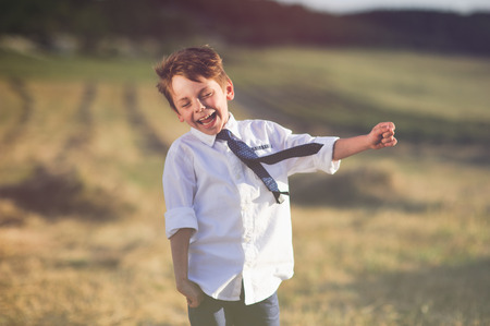 funny laughing little boy wearing white shirt and tie fluttering on blowing wind outdoorの写真素材