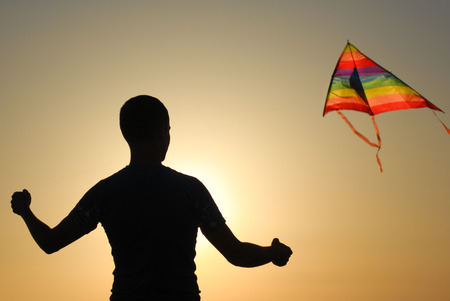 young man with colorful flying kite on summer warm sunset outdoorsの写真素材