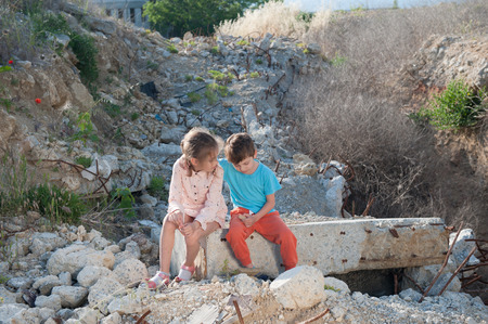 suffering fatherless caucasian boy and girl sitting on ruins of destroyed house in summerの写真素材