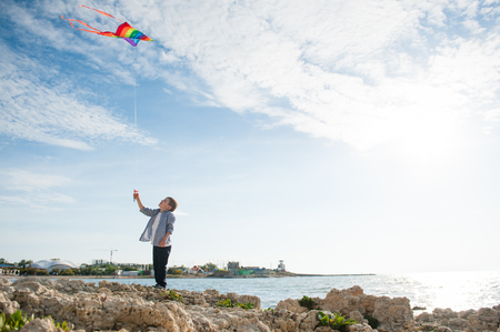 happy little caucasian boy with flying kite on sea town and sky background outdoorsの写真素材