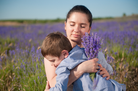 beautiful caucasian woman holding bouquet hugging her cute little son among lavender fieldの写真素材