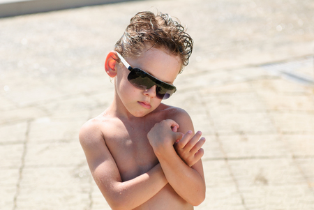 cute upset caucasian little boy in sunglasses with funny wet hairstyle and wet bodyの写真素材