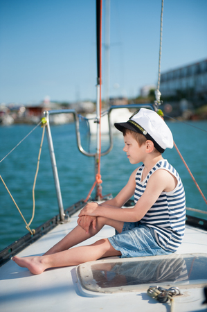 pensive small caucasian boy in captain hat sitting luxury yacht board watching far aheadの写真素材