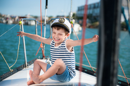 happy delightful kid in captain cap sitting on luxury yacht boardの写真素材