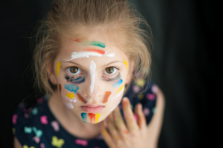 afraid pretty little girl with face painted with various colors copyspace on black backdrop