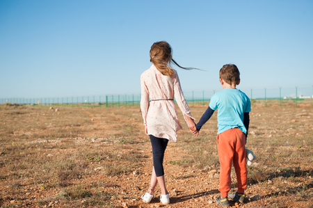 small brother and sister refugees holding hands standing among desert on state borderの写真素材