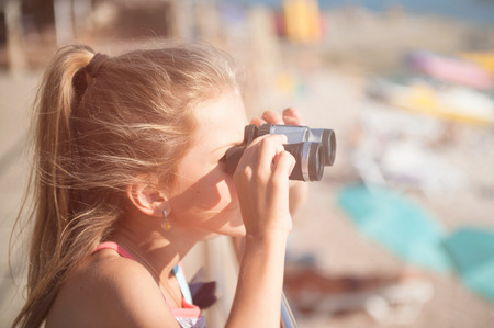 cute little caucasian girl holding binoculars watching far away on beachの写真素材