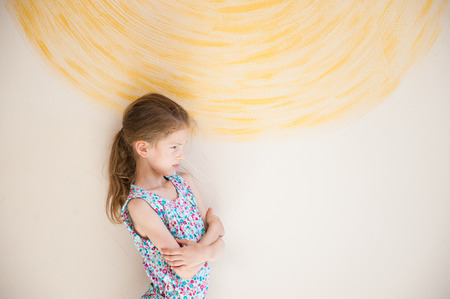 frustrated small girl with grimace on her face near yellow wall mental health indoorsの写真素材