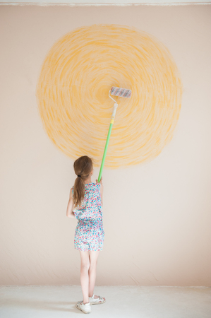 slim little artist caucasian girl painting yellow sun on wall with paint rollerの写真素材