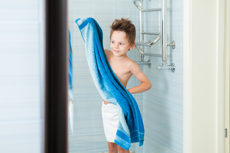 beautiful healthy kid dry off his body with blue towel in bright bathroomの写真素材