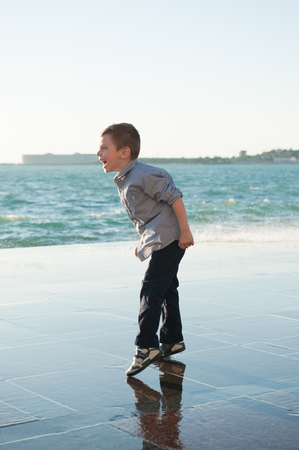 funny jumping little child shouting towards storm sea in port town in fallの写真素材