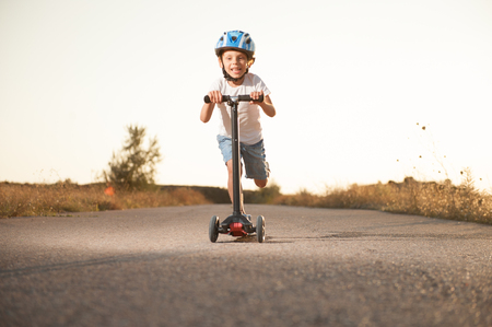 healthy little caucasian boy in helmet riding scooter on road with high speed outdoorの写真素材