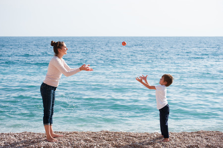 happy healthy family consisting of mother and child playing droping apple on beach in autumnの写真素材