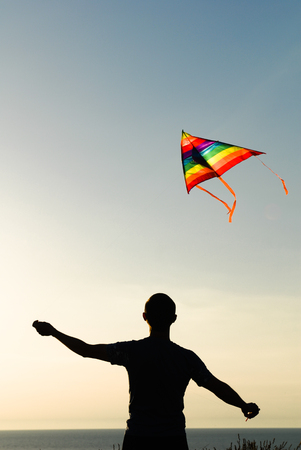 silhouette of active young man controling flying kite outdoors in sunsetの写真素材