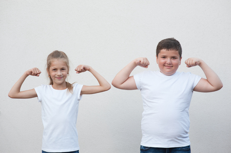 two children little thin girl and thick boy showing their muscle on copyspace backgroundの写真素材