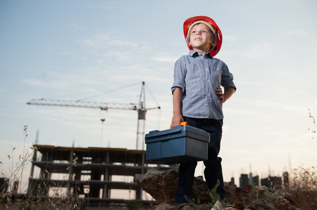 cute little kid in builder helmet with toolbox in hand on standing construction siteの写真素材