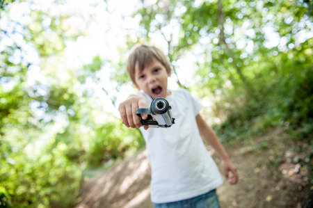 angry threatening little caucasian kid aiming gun at camera shouting outdoorsの写真素材