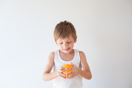 healthy small caucasian kid in white shirt holding orange fruit on white backgroundの写真素材