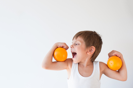 hungry healthy cute little caucasian boy wants to eat orange on his biceps muscleの写真素材