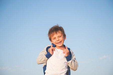 happy delightful smiling caucasian little boy in sweater on blue sky backgroundの写真素材