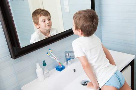 handsome healthy small caucasian boy watching at his reflection in mirror in bathroomの写真素材