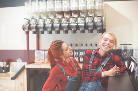 two modern trendy young girls laughing sitting in coffee shop indoorsの写真素材