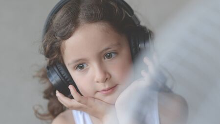 beautiful little curly little girl in headphones with hair blown with wind from cooling fun listen...