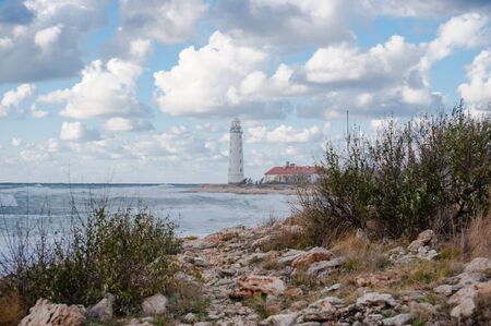 outdoor landscape with sea stormy shore and white beacon on horizon with beautiful cloudsの写真素材