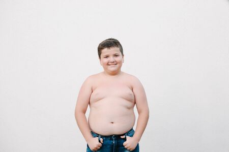 happy smiling fat little kid in jeans standing on bright wall background with copy spaceの写真素材
