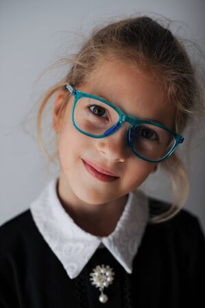 wunderkind little girl in blue eyeglasses and school black and white uniform smiling portraitの写真素材