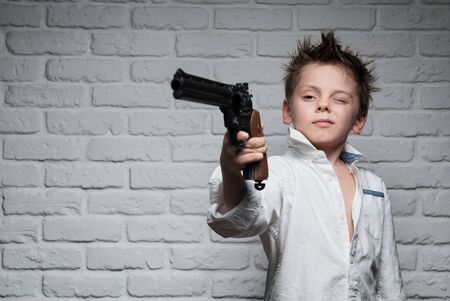 cute little kid in white shirt holding long revolver gun pointing at target on brick wall backgroundの写真素材