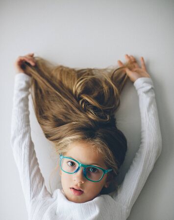 beautiful little caucasian girl in blue glasses holding her long blonde hair upの写真素材