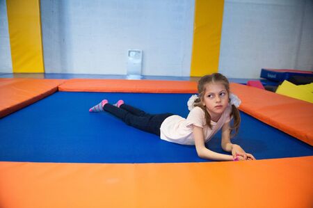 cute slim healthy little girl lying on trampoline indoorsの写真素材