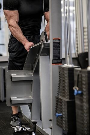 sport equipment concept of strong muscular man in black sportswear training on fitness machine...