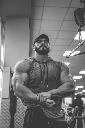 black and white photo of young strong man with beard posing in fitness gym