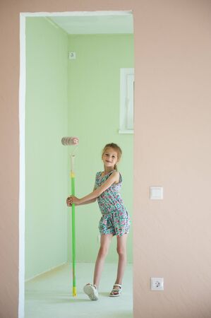 beautiful thin little girl stand with paint roller in new flat apartmentの写真素材