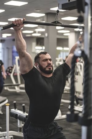 heavy weight lifting training in sport gym by young bearded man in black shirt pumping ironの写真素材