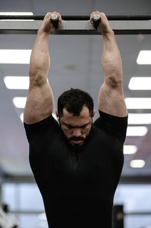 strong young man wearing black jersey and beard stretching muscles on chin ups barの写真素材
