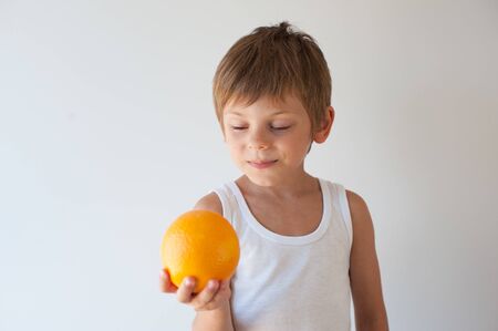 one cute smiling healthy little kid holding fresh orange in hand on bright white backgroundの写真素材