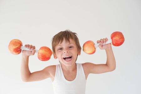 happy delightful active strong small laughing kid in tank top lifting dumbbells made from apple fruitsの写真素材