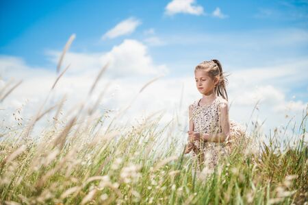beautiful little thin girl in summer dress in grass field under blue cloudy skyの写真素材