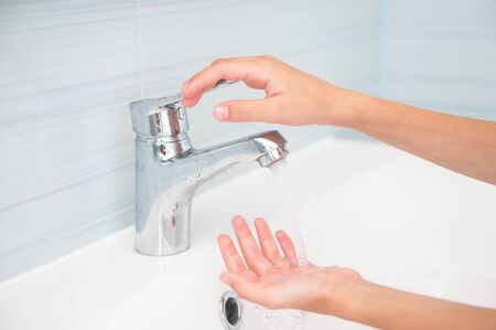 thin child small hands opening faucet with flowing water in bathroomの写真素材