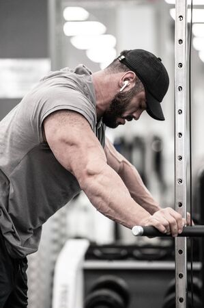 tired relaxing young strong man with beard resting during heavy weight training workout in sport gym listening music in wireless headphonesの写真素材