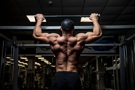 strong young man lifting his heavy weight body during chin ups on horizontal bar in sport gym
